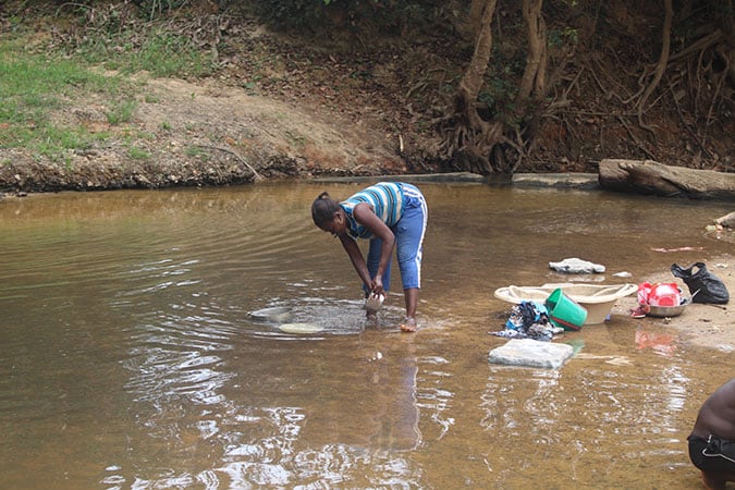 Water: Carrying the Burden - Woman Washing Dishes in Dirty Water